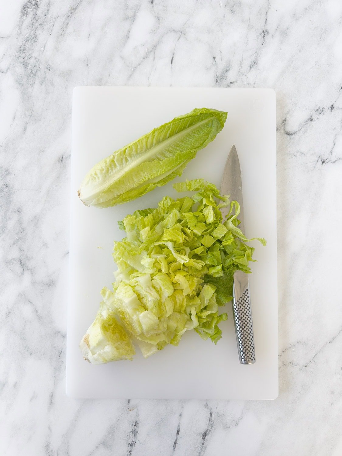 Chopping hearts of Romaine lettuce on a cutting board with a chef's knife.