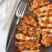 Bright red orange Buffalo grilled chicken breasts on a gray platter with a serving fork.