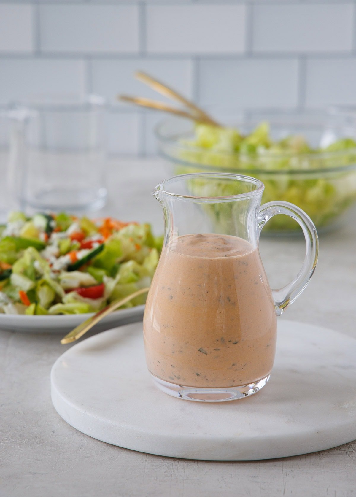 A glass cruet of creamy orange buffalo ranch dressing with a salad near by.