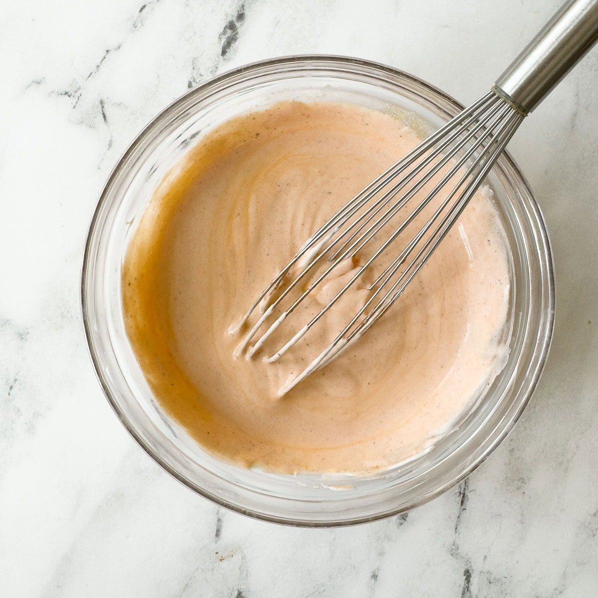 Creamy light orange buffalo dressing being made in a bowl with a whisk.
