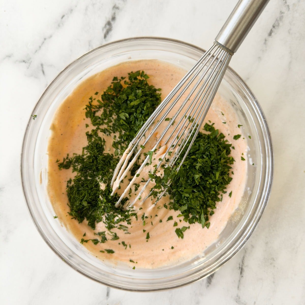 Adding fresh chopped green herbs to a bowl of buffalo ranch dip.
