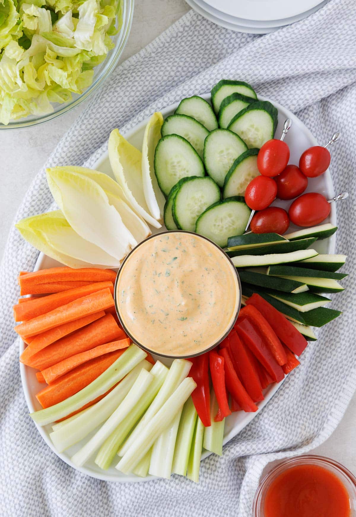 A platter of colorful fresh cut veggies with buffalo ranch in the center bowl.