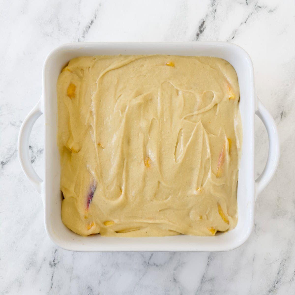A white baking dish spread over the top with creamy batter for a cobbler.