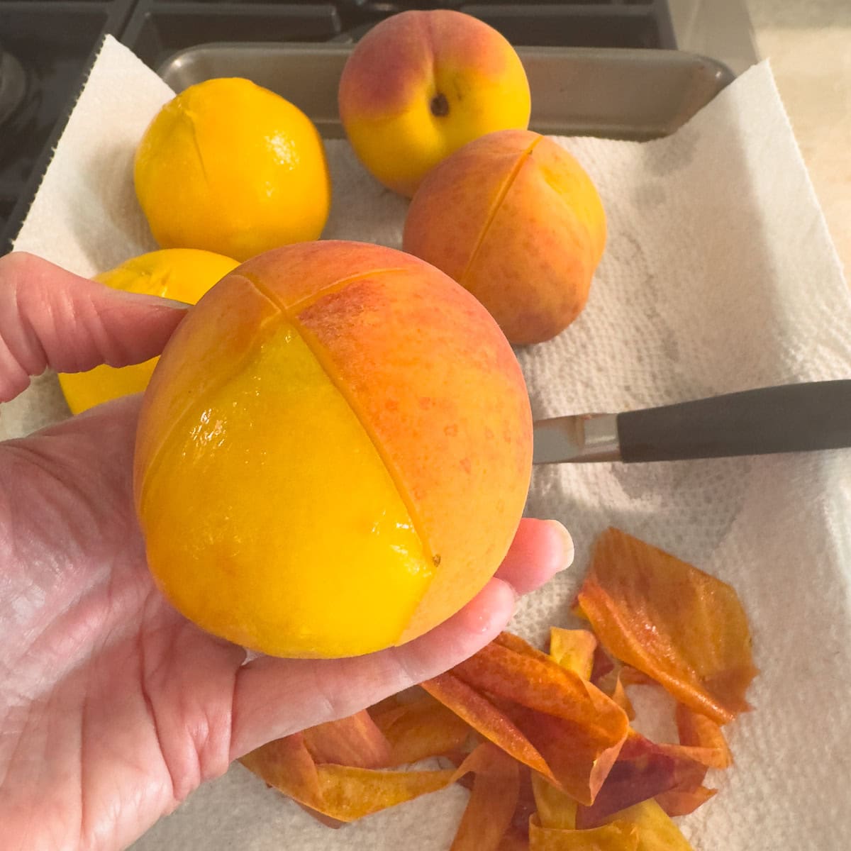 A peeled peach after blanching with peeled peaches in the background.