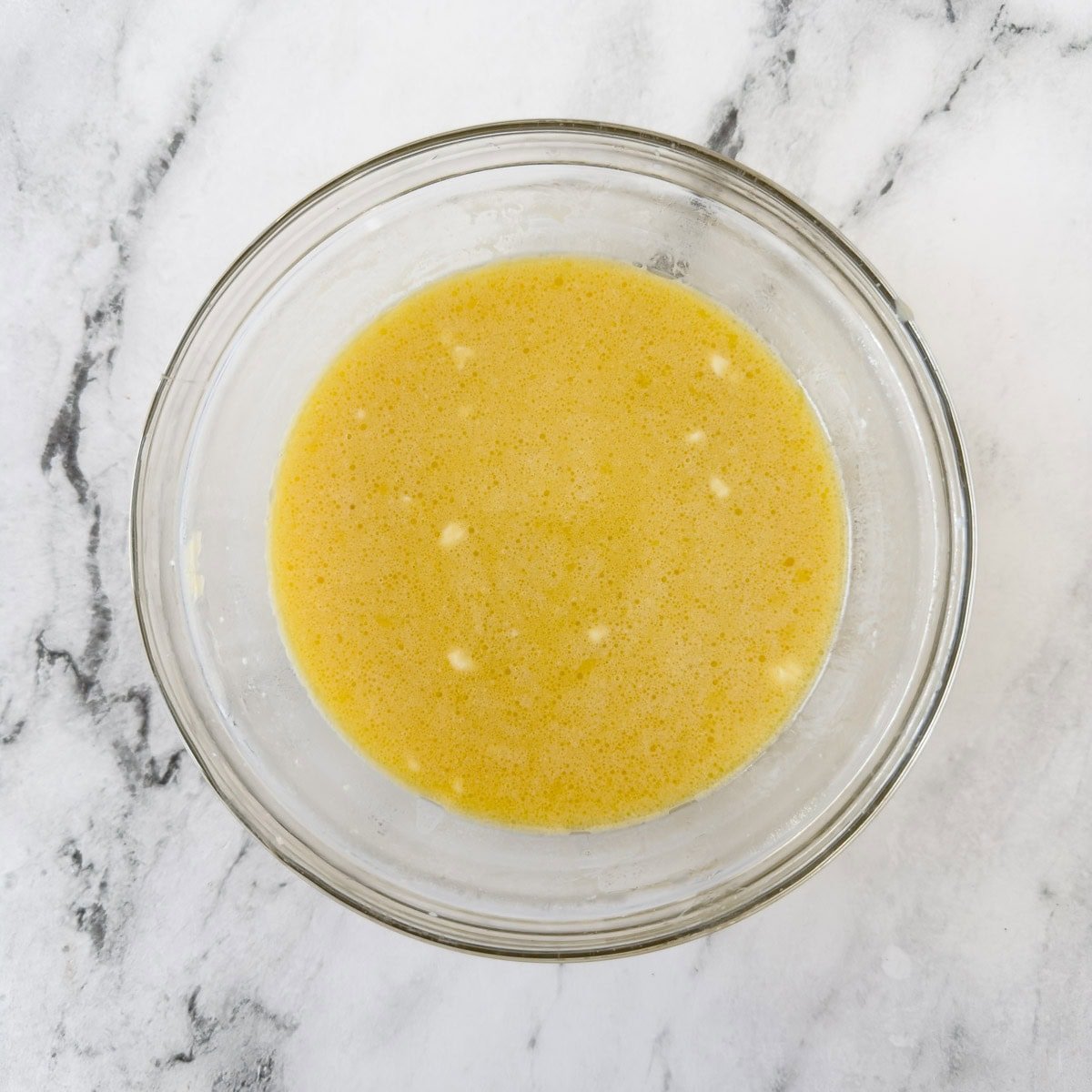 A glass bowl of eggs, milk and melted butter.