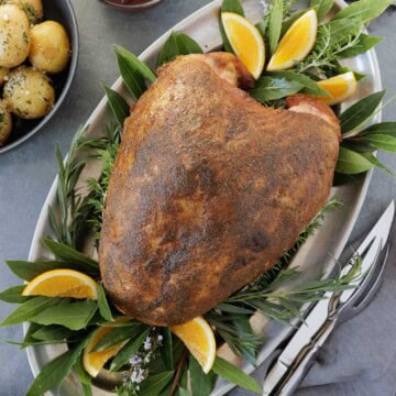 A browned, whole smoked turkey breast in a silver platter with bay leaves, potatoes on side,