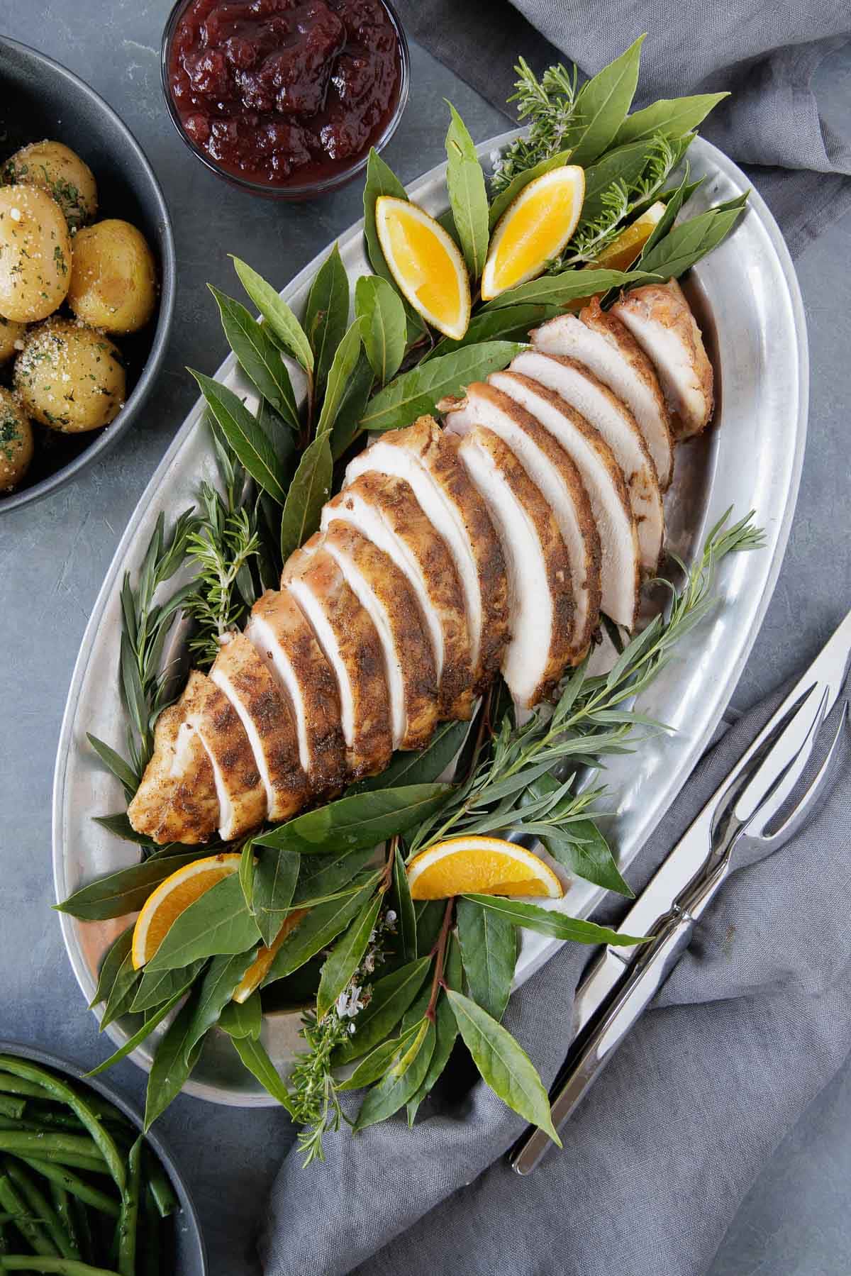 A sliced smoked turkey breast on a pewter platter with bay leaves and orange wedges.