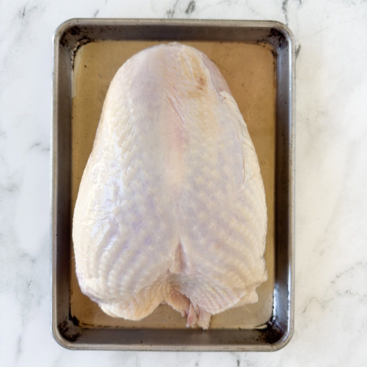 A raw whole turkey breast on a parchment covered sheet tray for perp.

