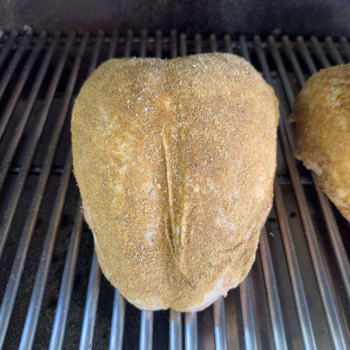 Seasoned whole turkey breast on the grill for smoking.