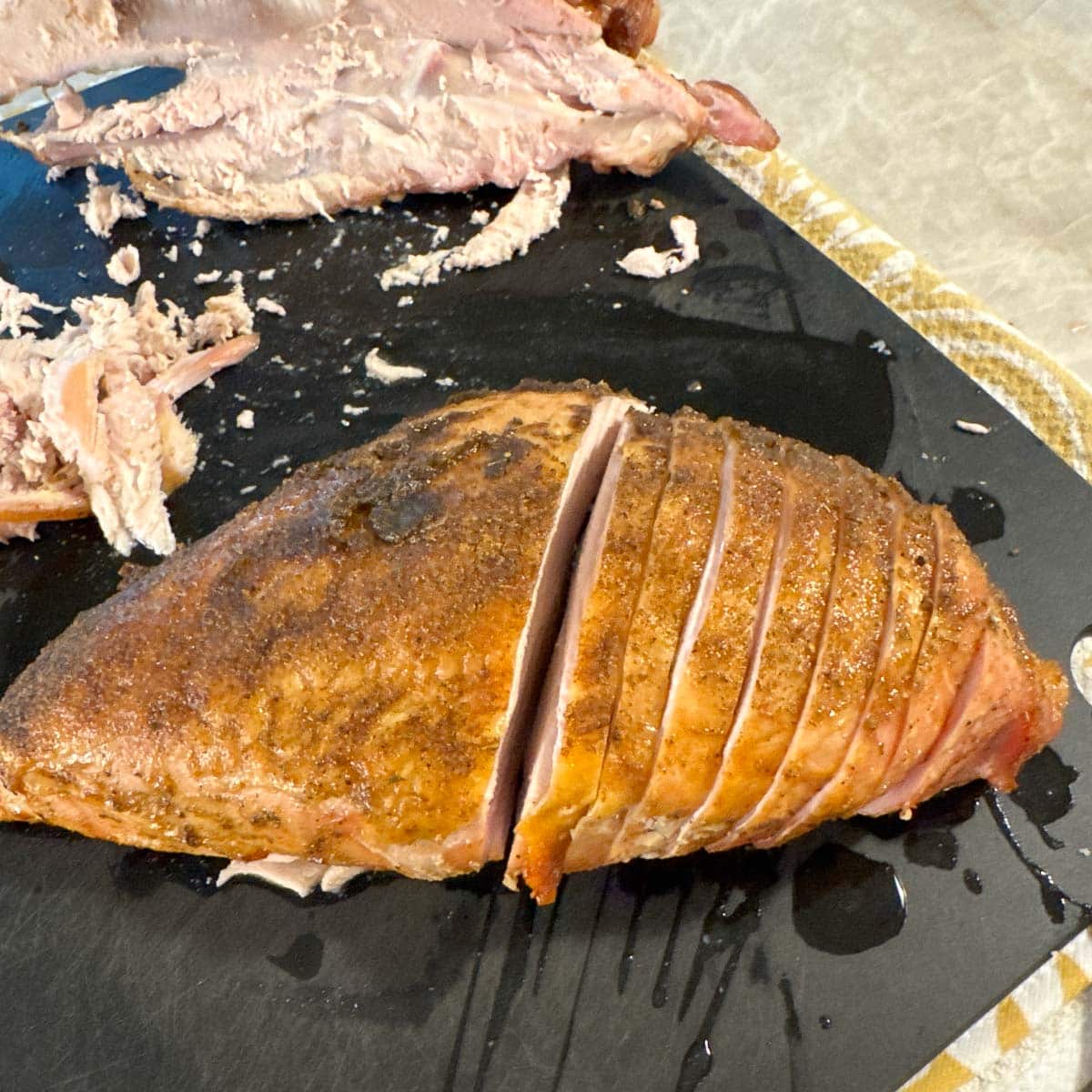 Half of a smoked turkey breast sliced on a black cutting board.