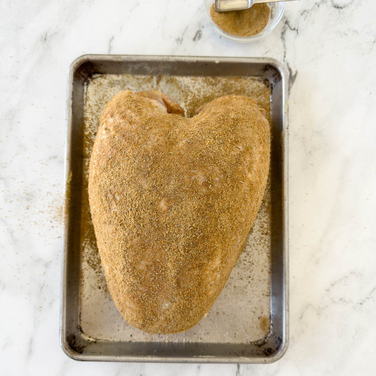Turkey breast covered in dry rub seasoning on a baking tray.