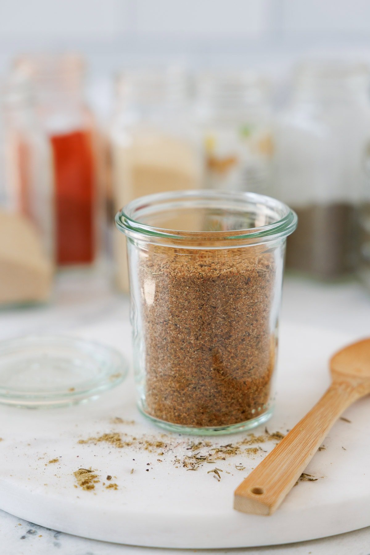 A jar of colorful turkey seasoning blend with a wooden spoon, spices jars in the back.