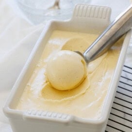 A scoop of cream vanilla bean ice cream on a silver ice cream scooper.