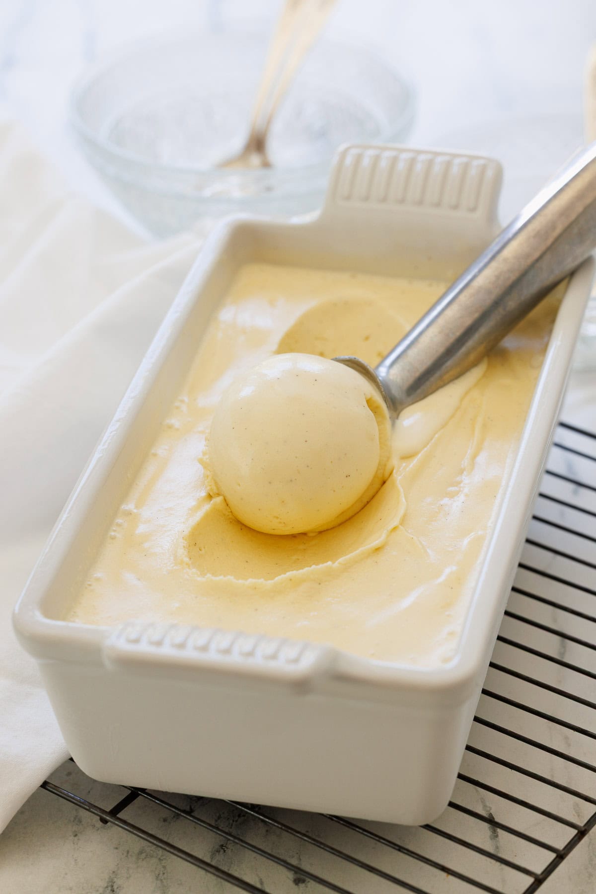 A perfect scoop of vanilla bean ice cream in a white ceramic loaf pan with silver scooper.