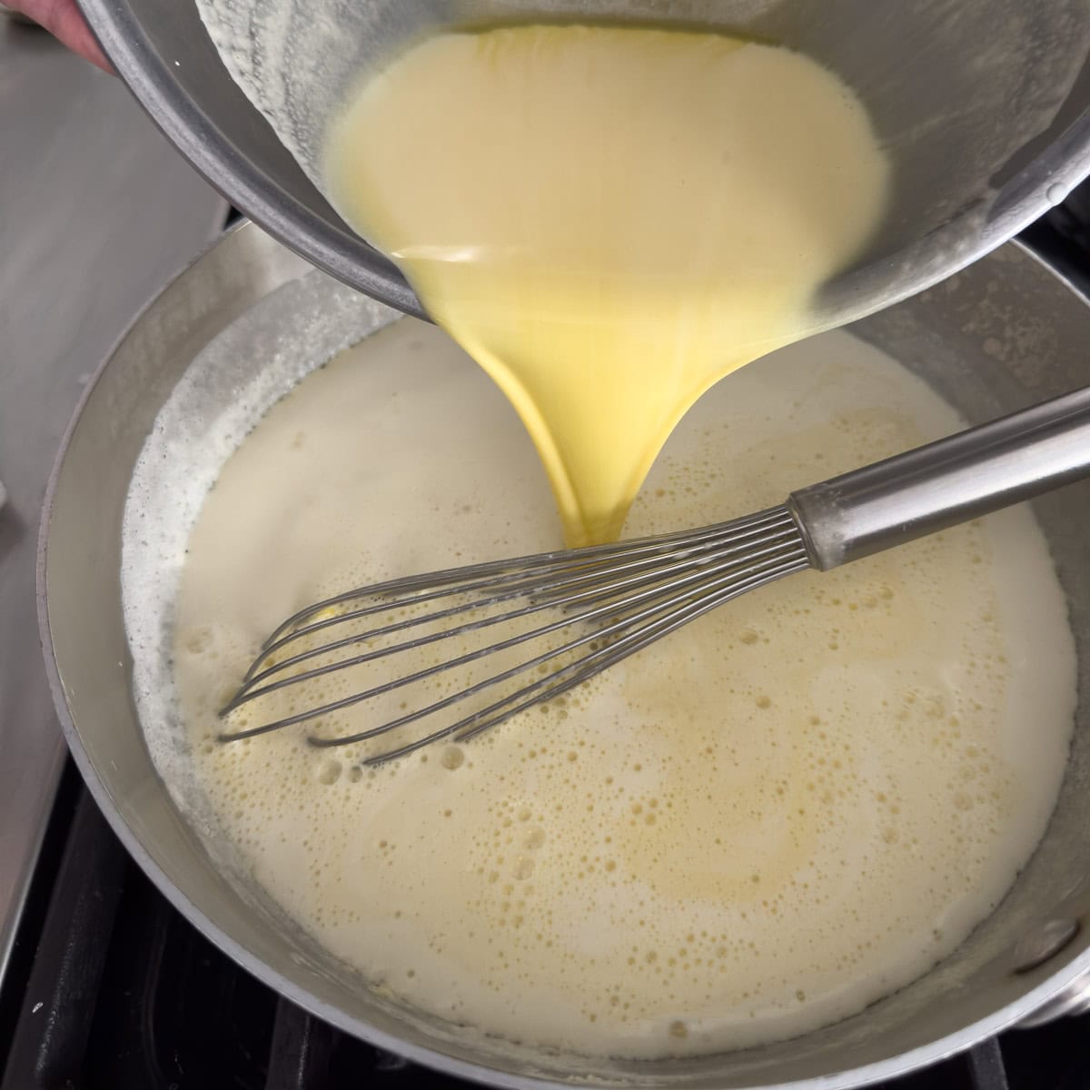 Pouring cooked egg yolks and cream into a stainless steel pan for cooking an ice cream base.