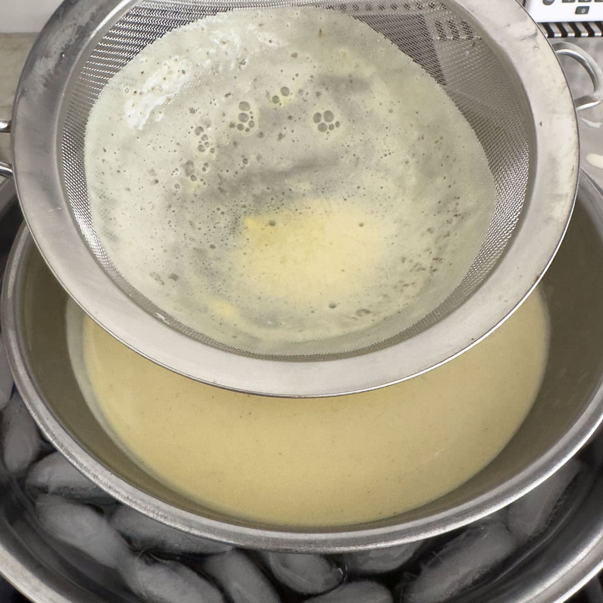 Straining custard through a sieve into a bowl in an ice bath.