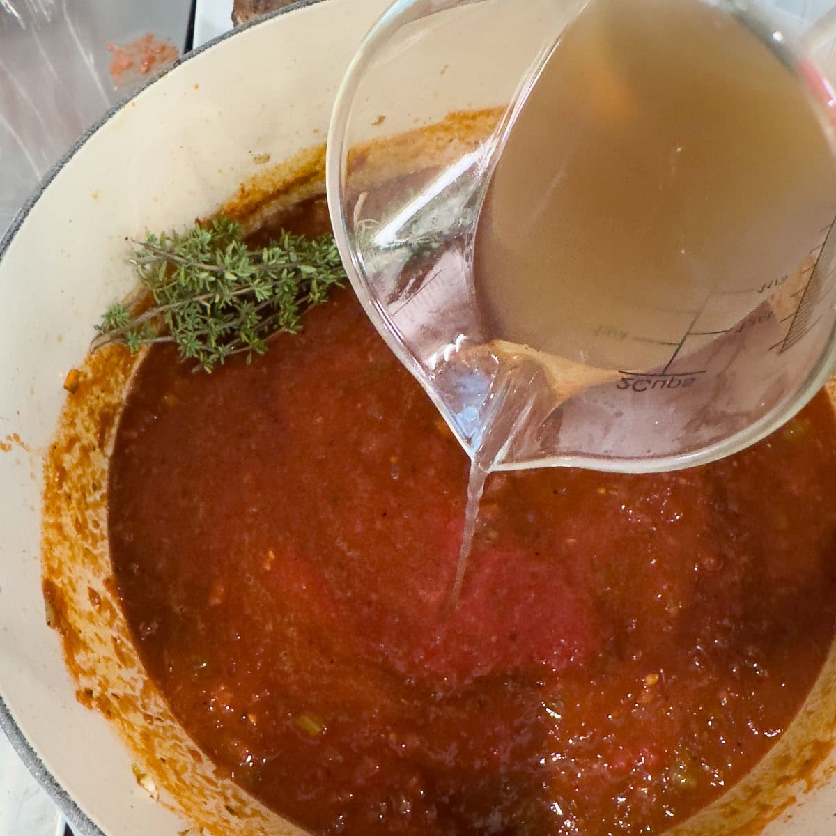 Broth being poured into a pot with vegetables and tomatoes. 