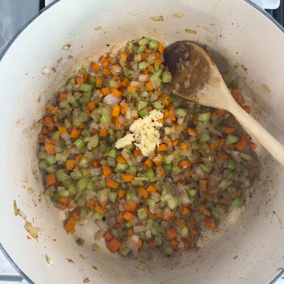 Carrots, onion, celery and garlic cooking in a pot with wooden spoon.