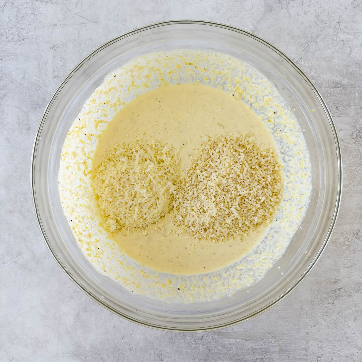 Adding grated cheese to a bowl of corn casserole batter. 