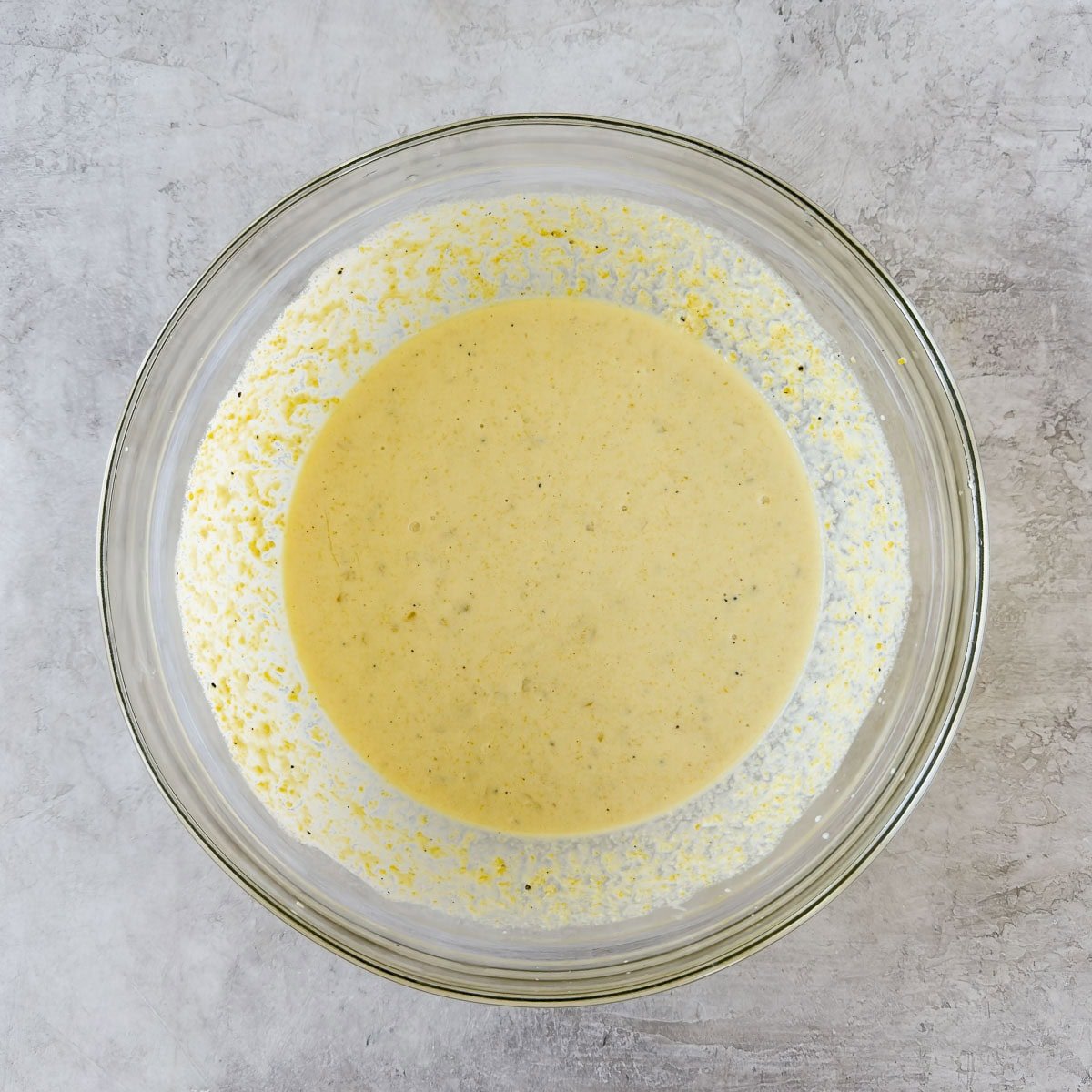 A bowl of corn souffle batter with corn kernels and half and half.