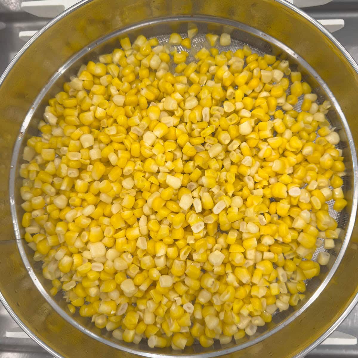 Draining bright yellow corn after cooking through a silver sieve.