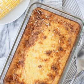 Golden corn souffle in a glass baking dish on a gray plaid kitchen towel.