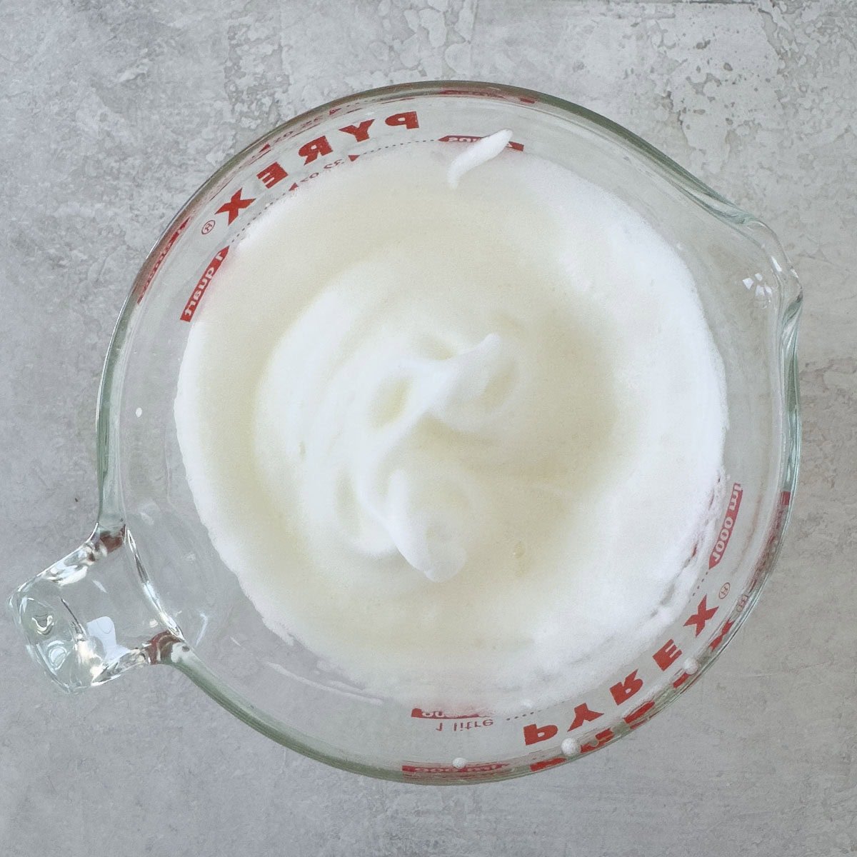 Softly whipped egg white in a large glass measuring container. 