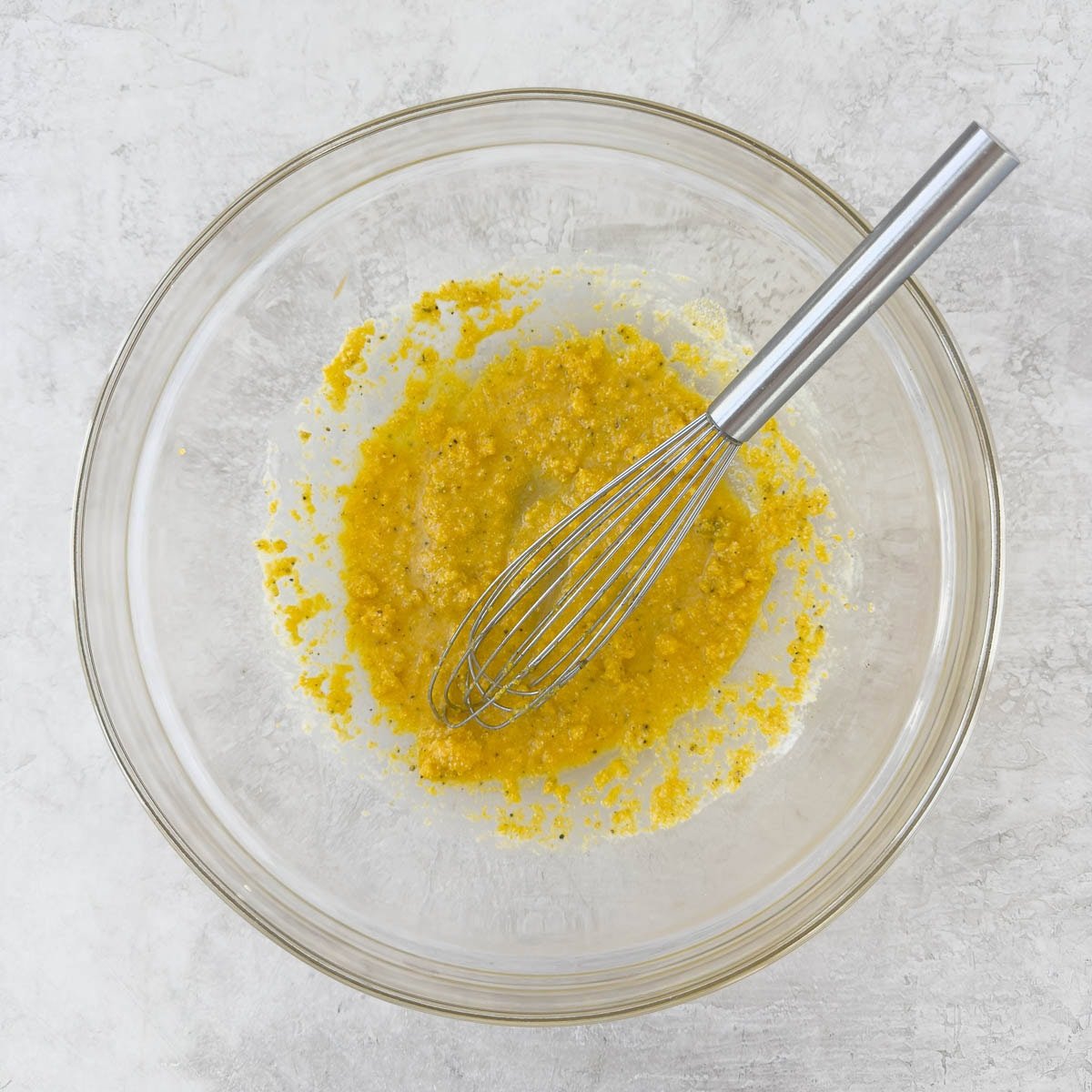 Glass bowl with cornmeal and silver whisked being mixed.