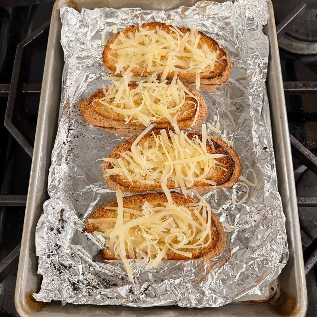 Garlic cheese toast ready for broiling on foil lined tray.
