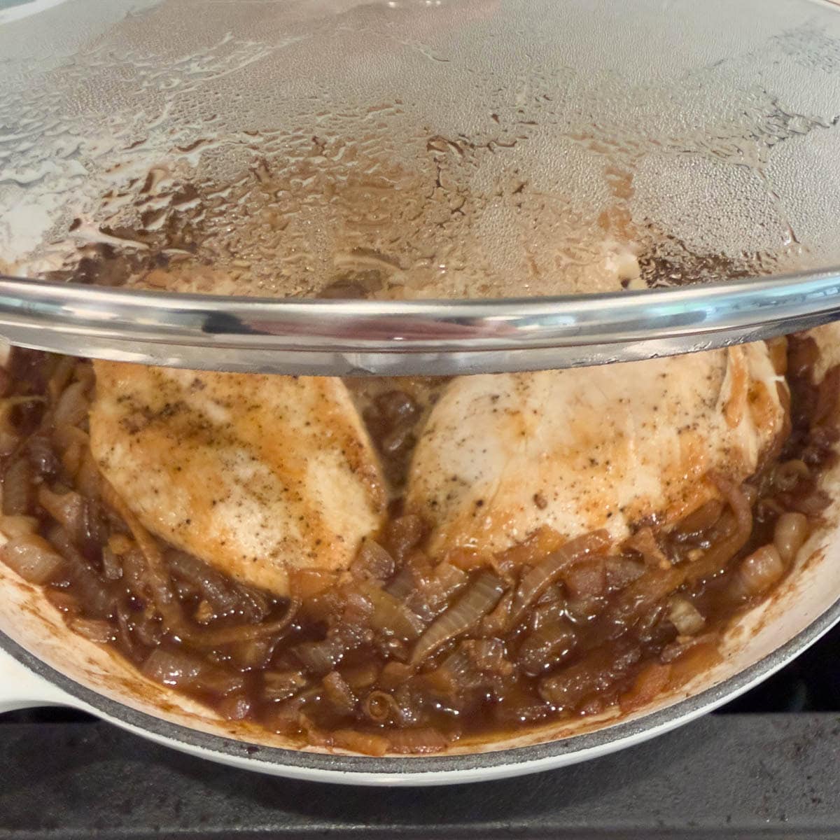 Placing a lid on a pan full of chicken and caramelized onions for french onion soup chicken.
