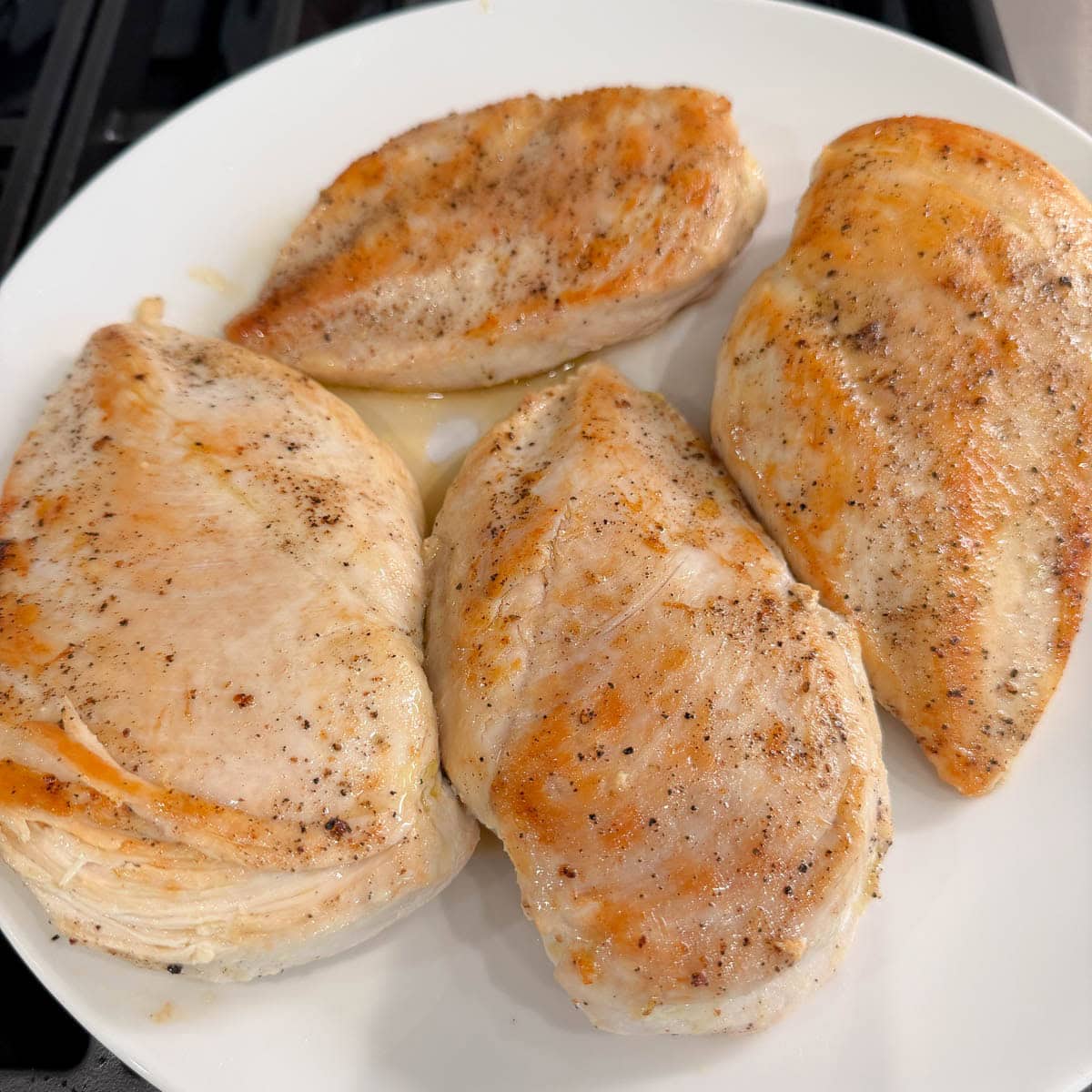 Browned chicken breasts on a white plate on a stovetop.