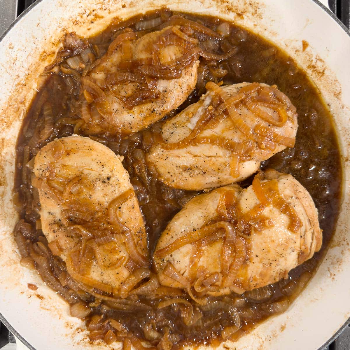 A finished pan of french onion chicken with deep brown caramelized onions. 