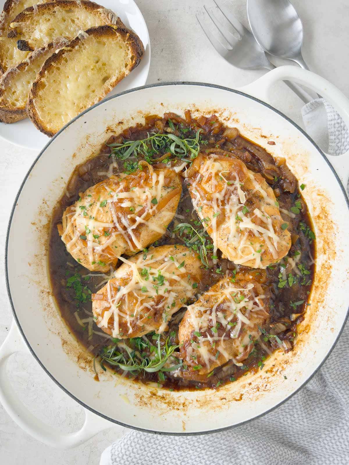 A shallow pan of French onion soup chicken with melted cheese, herbs, and cheesy toasts.