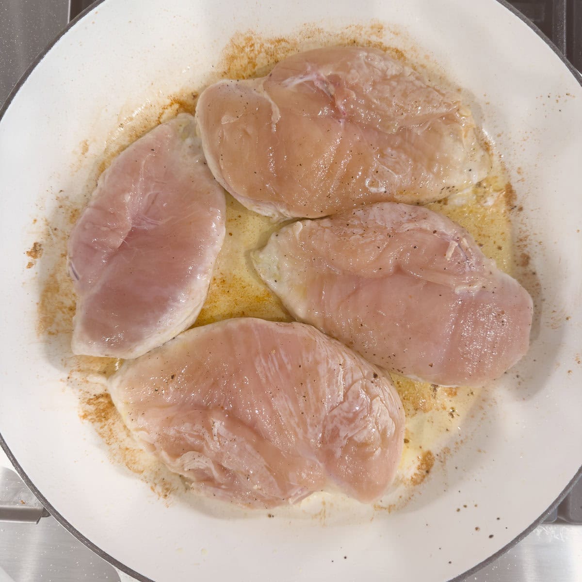 Cooking boneless chicken breasts in a white shallow pan in olive oil.