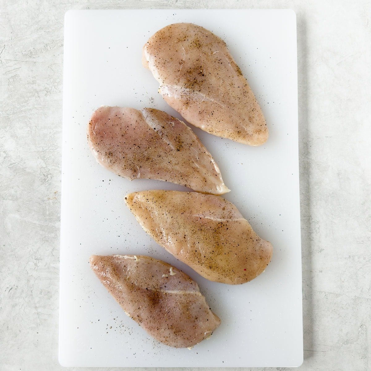 Seasoning boneless chicken breasts with salt and pepper.
