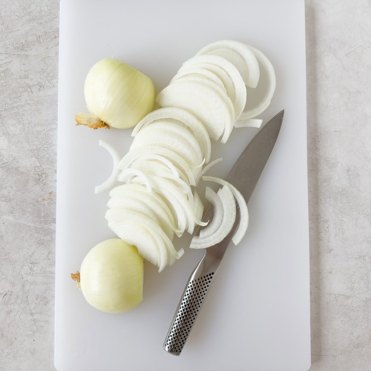 Slicing onions for french onion chicken on a white cutting board.