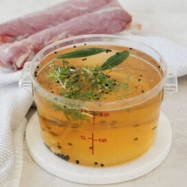 A container of golden brine with herbs, and garlic for brining pork.