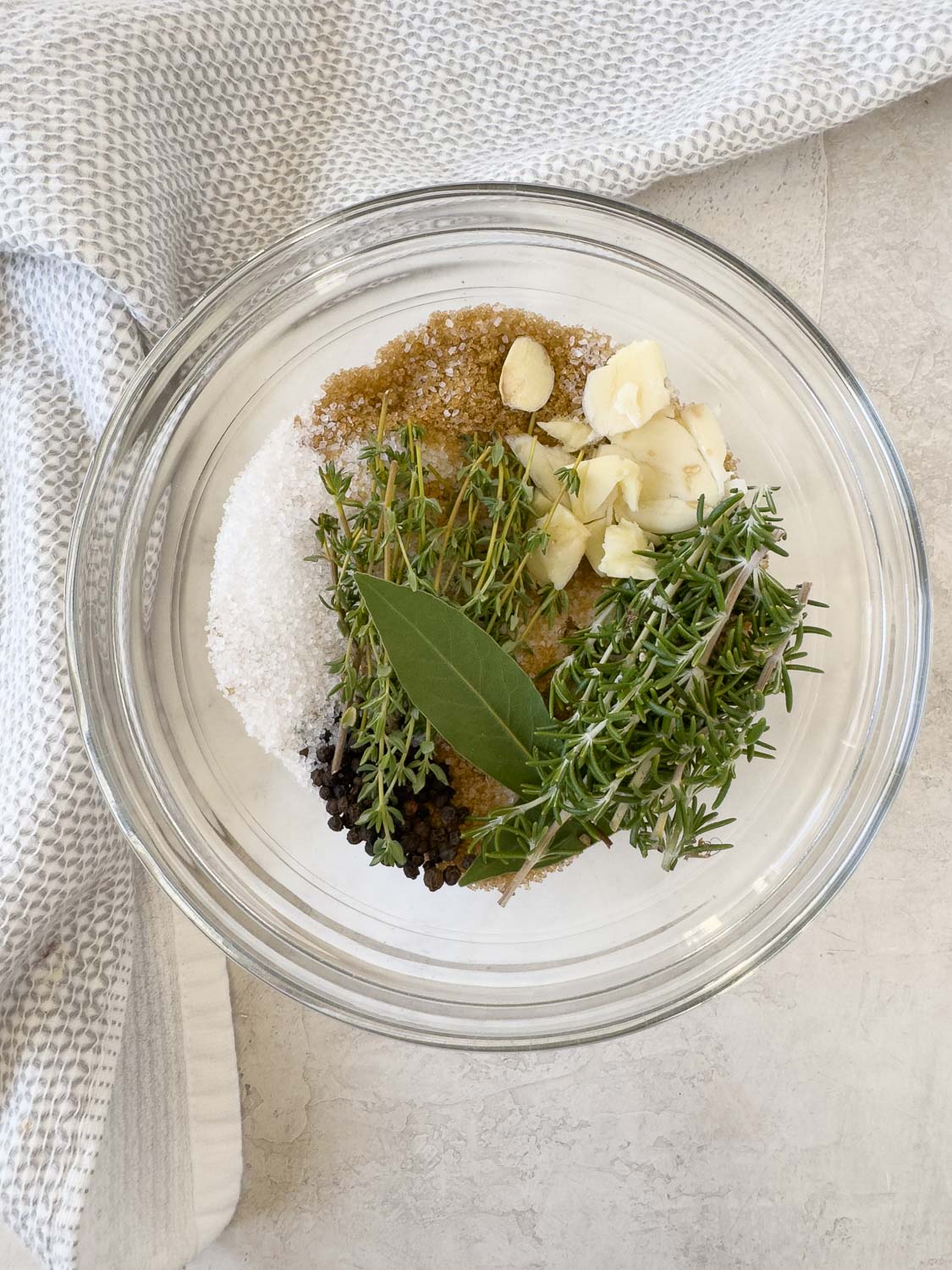 Salt, brown sugar, bay leaf, herbs, garlic and peppercorns for pork brine in a bowl.