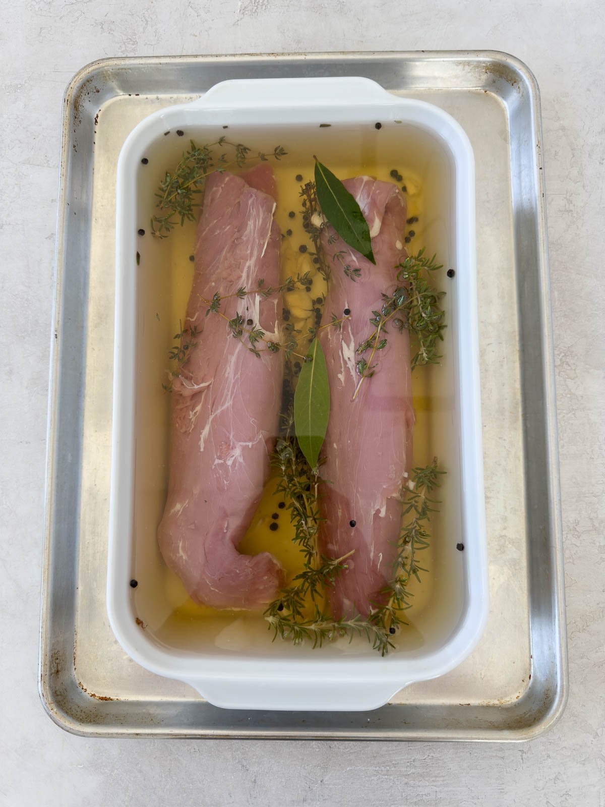 Two pork tenderloins submerged in a pork brine in a shallow casserole dish. 