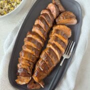 BBQ glazed smoked pork tenderloin sliced on a gray platter for serving.