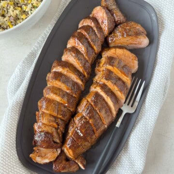 BBQ glazed smoked pork tenderloin sliced on a gray platter for serving.