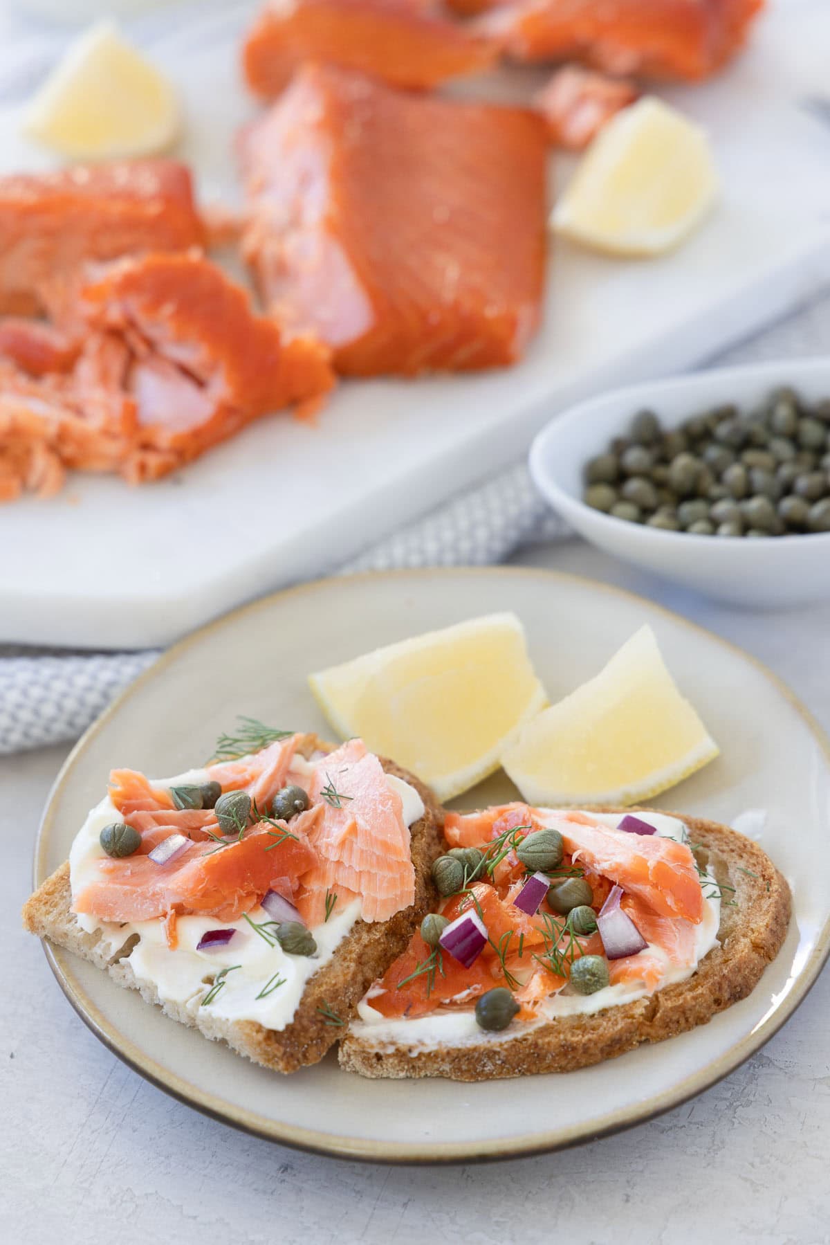 Appetizer plates of smoked salmon on bread with whipped ricotta, capers, dill, and red onion.