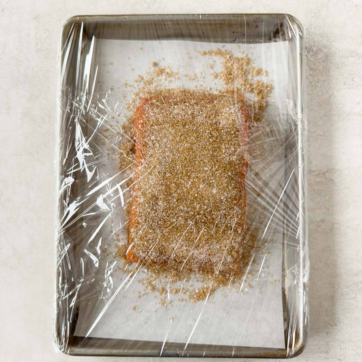 Plastic wrapped salmon filet covered in smoking cure for the curing phase.
