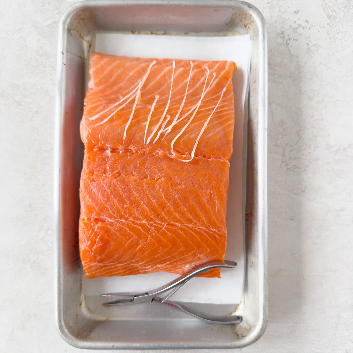 Bright orange salmon filet showing pin bones removed on a metal tray.
