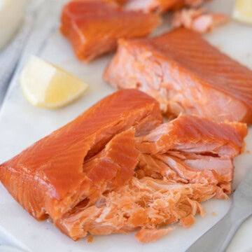 Flaked smoked salmon from a pellet grill on a serving board with lemons.