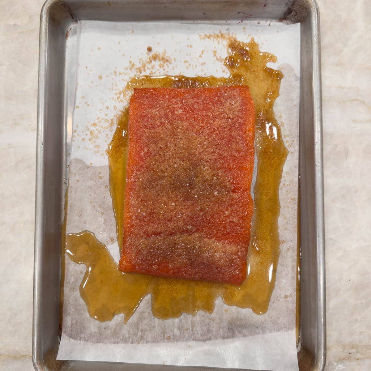 Salmon filet after curing with sugar and salt with excess liquid on tray.