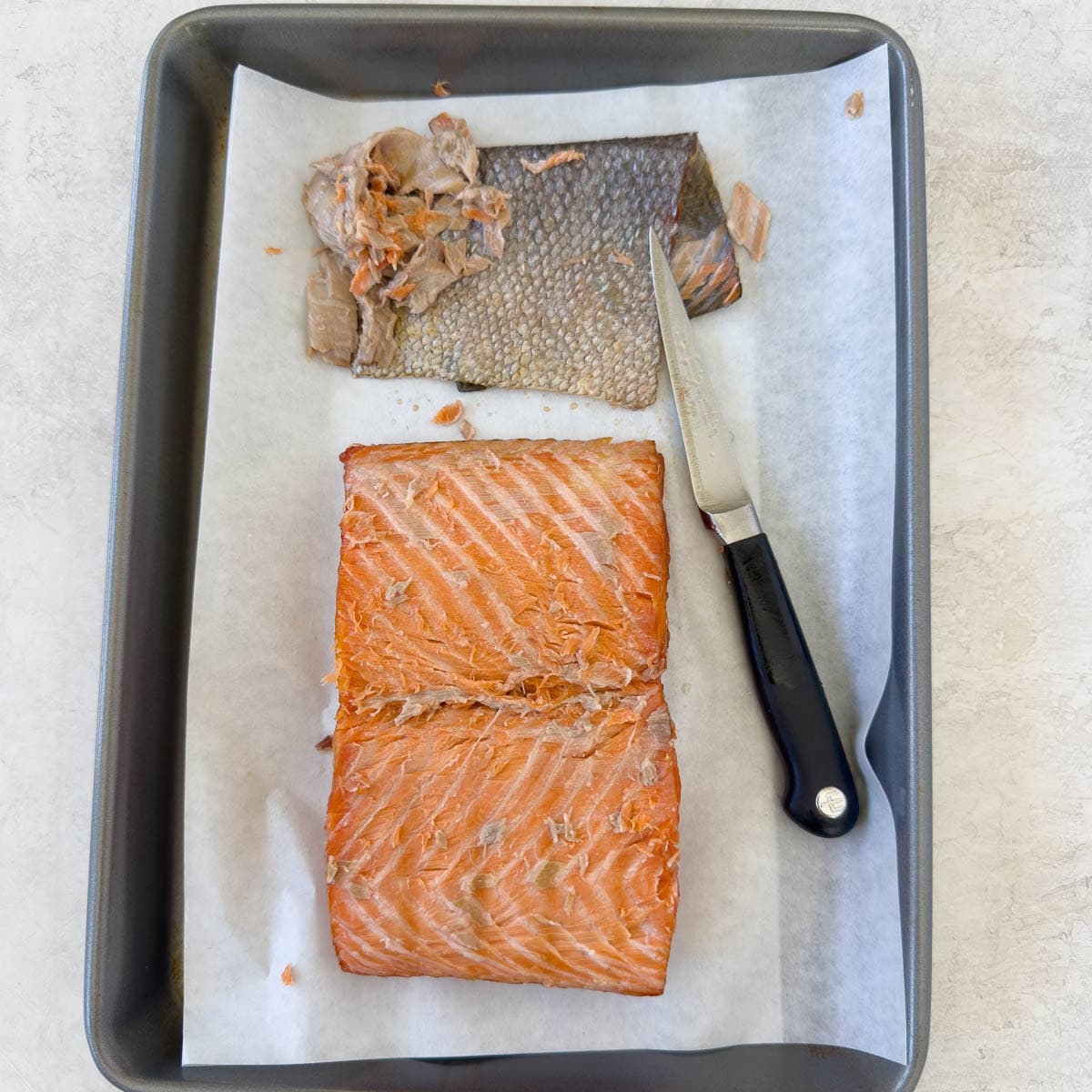 The bottom of a smoked salmon fillet being skinned and trimmed. 