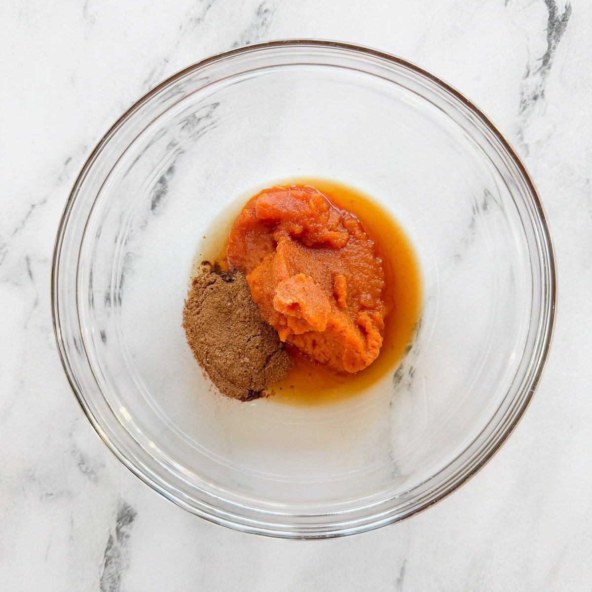 Spices, pumpkin, and  maple syrup in a glass bowl.