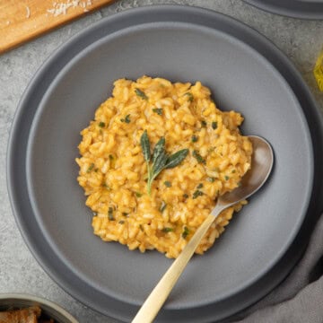 A gray bowl of pumpkin risotto with a golden spoon and sage leaves.