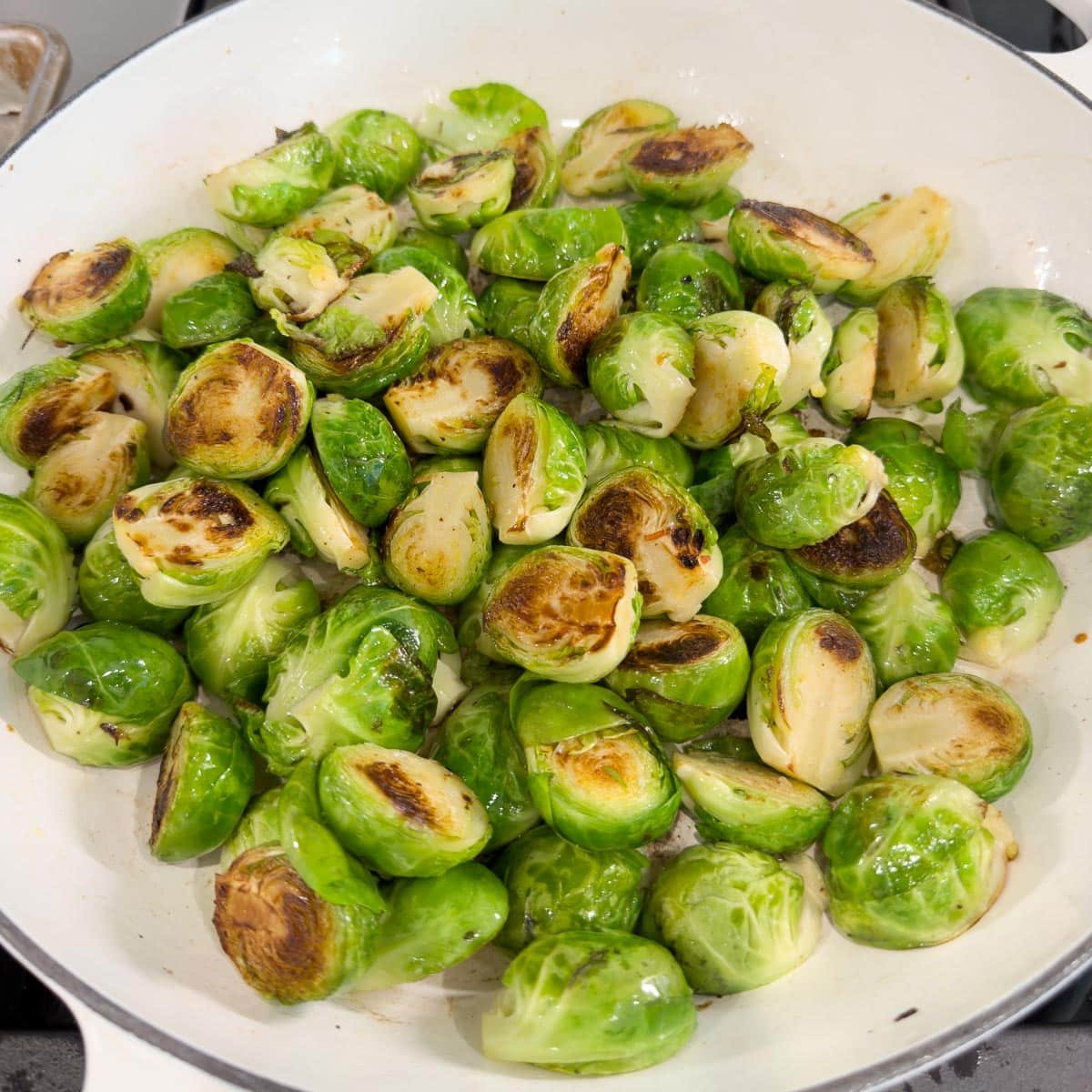 Browned and glossy Brussels sprouts in a wide white skillet.